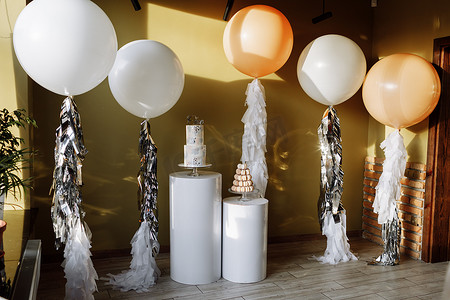 用两层楼的蛋糕和带金属丝的白色和米色大气球装饰一岁生日。