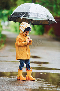 防水雨伞摄影照片_雨后穿着黄色防水斗篷、靴子和雨伞在户外玩耍的孩子