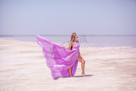 一位身穿粉红色连衣裙的女士沿着白色的咸水湖岸漫步，欣赏粉红色盐湖的美景，留下难忘的回忆。