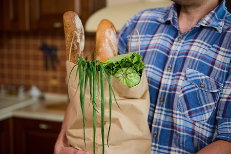 一个生态纸购物袋的剪影，里面有全麦面包，男人手里拿着健康的素食食品