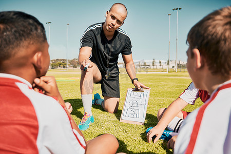 儿童足球队摄影照片_足球队、儿童和带剪贴板的教练在谈论锻炼计划、训练和战术时在户外足球场进行健身、比赛和运动。