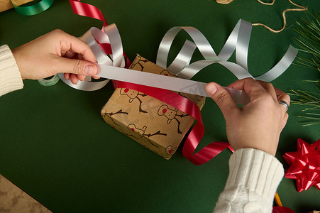顶视图的女人拿着红白相间的闪亮丝带，在包装礼品纸上，为圣诞节或新年包装礼物