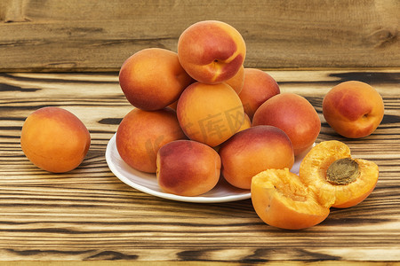 在一张木桌上和一个白色的碟子上，放着成熟的杏子