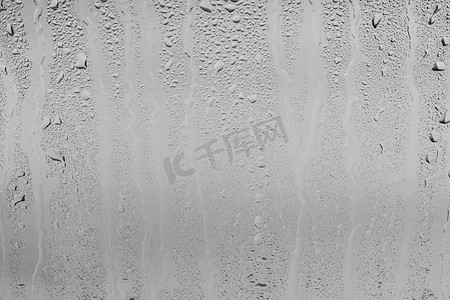 透明灰色背景摄影照片_灰色天空背景下的雨滴落在窗户玻璃表面上。