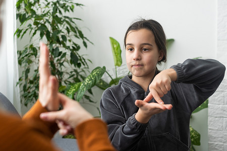 可爱的小女孩与妈妈或女保姆做手势学习手语，微笑的小孩在家与老师练习非语言交谈，学龄前残疾儿童与导师上课