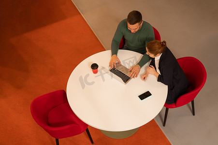 在圆桌会议上使用笔记本电脑工作的男人和女人的顶视图。