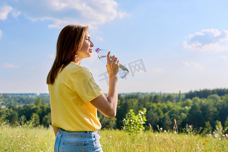 炎热的夏日，口渴的成年女性在大自然中从瓶子里喝水给我们