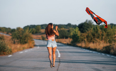 黑色的风筝摄影照片_年轻快乐的女人在户外的路上玩风筝