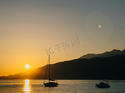 海上帆船运动摄影照片_帆船停泊在海上以日落山为背景
