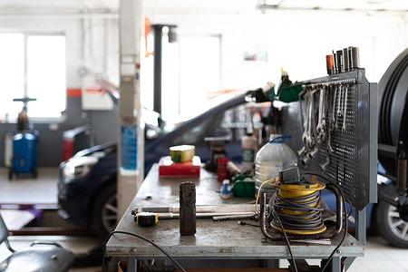 一张金属桌的照片，上面有用于工作和修理汽车的工作工具，背景是服务站一辆蓝色客车正在用敞篷修理