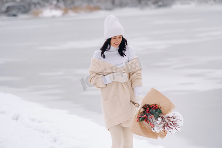 冬花摄影照片_一个穿着米色开衫和冬花的女孩在下雪的季节在大自然中漫步。