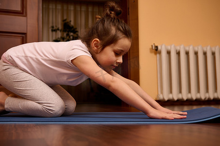 特写小女孩在 Balasana 姿势中伸展身体，坐在儿童姿势中，同时在健身垫上练习瑜伽