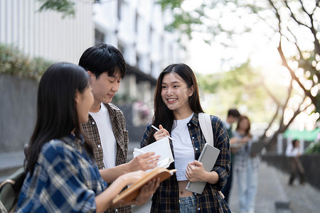 记事本摄影照片_一群亚洲大学生在户外草地上阅读书籍和辅导特殊课程。