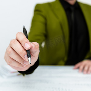 身穿绿色西装的男模特坐在白桌旁，用笔指着重要信息。