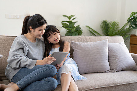快乐的亚洲女人向在家拥抱她的女儿展示数字平板电脑。