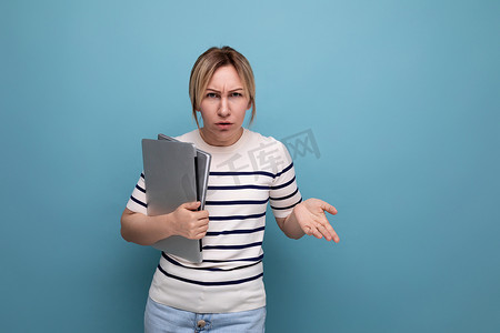 条纹毛衣摄影照片_蓝色背景下，一位身穿休闲条纹毛衣、手里拿着便携式电脑笔记本电脑的愤怒女商人的水平照片