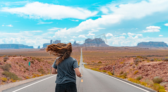 从后面看有魅力的年轻女人在沙漠中的美国直路中间奔跑。