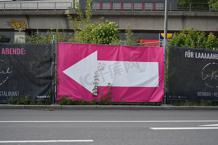 带有粉红色海报和指向左侧的白色箭头的广告牌
