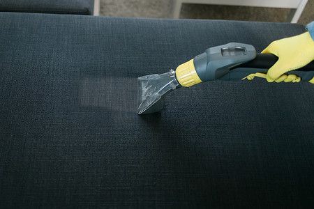 戴防护橡胶手套清洁沙发的男子用专业提取方法用洗涤真空吸尘器清洁沙发。