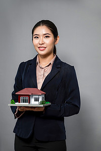 穿着正式西装的年轻亚裔女性拿着房子模型。