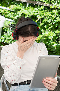 女孩忧郁摄影照片_悲伤的女孩在咖啡馆的桌子旁听平板电脑上的音乐