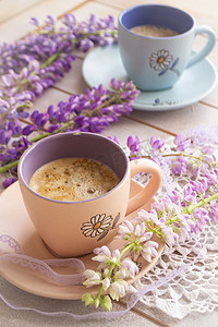 咖啡豆花摄影照片_杯咖啡和羽扇豆花在白色的木桌上。