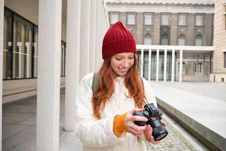 拍照脸摄影照片_漂亮的读头女孩，带专业相机的摄影师在户外拍照，在城市里走来走去，拍照，观光