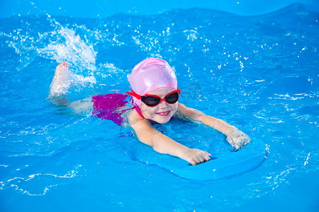 微笑的小女孩在游泳课上用颤音板在室内游泳池里学习游泳