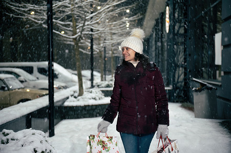 在一个多雪的冬夜，穿着暖和的衣服，带着购物袋，走在城市街道上的令人愉快的多民族女性