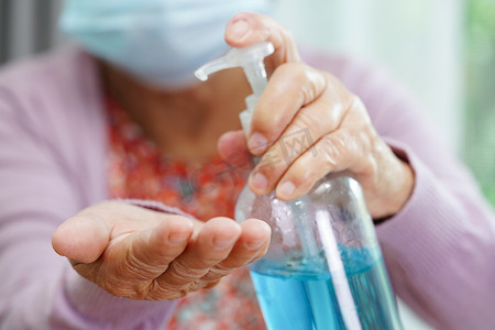 消毒凝胶摄影照片_亚洲老年妇女按蓝色酒精消毒凝胶洗手保护感染冠状病毒。