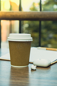 在工艺回收纸杯中的热拿铁咖啡，纸质笔记本和无线耳机。