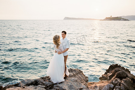 日落时分，新郎在海边的岩石上拥抱新娘