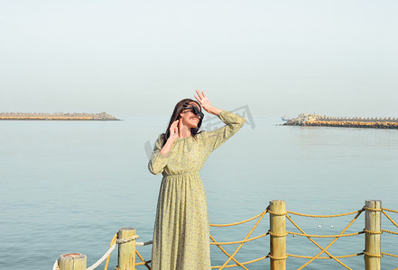 女孩望天空摄影照片_一位身穿长裙的年轻美女独自站在海边的码头上，望着太阳。
