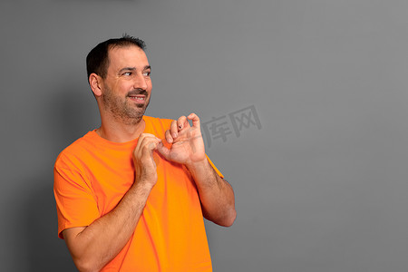 尴尬表情摄影照片_留着胡子的西班牙裔男子身穿橙色 T 恤，面带害羞和尴尬的表情看着旁边。
