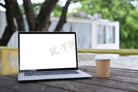 在室外的木桌上模拟电脑笔记本电脑和咖啡杯。