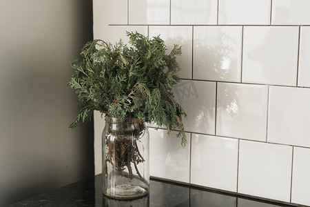秋天花瓶摄影照片_杜松的绿色分支在厨房的玻璃花瓶里。