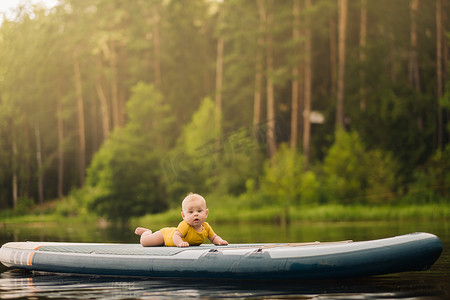 漂浮在水面上摄影照片_孩子躺在一个大的支撑板上漂浮在水面上。