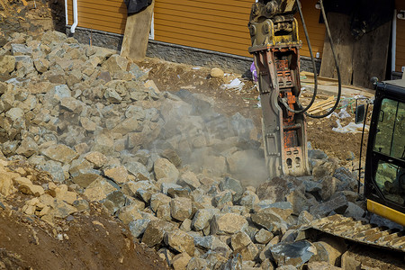 锤石摄影照片_一种带有手提钻和液压锤的挖掘机，用于用液压锤粉碎大量石块进行筑路