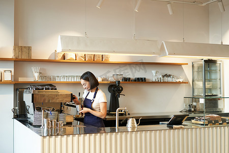 咖啡馆柜台的画像，咖啡师女孩用咖啡机工作，为店里的顾客下订单，穿着蓝色围裙