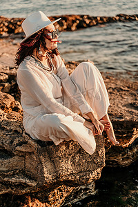 一位穿着白色裤装和帽子的女人站在沙滩上享受大海。