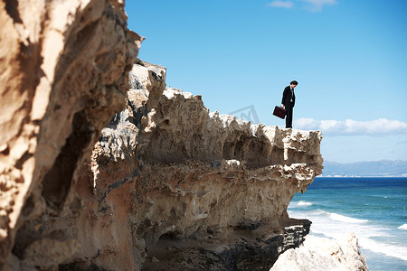 它很长的路要走......拿着公文包的商人站在悬崖上俯视着大海。