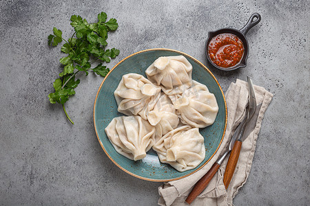 盘子上的格鲁吉亚饺子 Khinkali 配有红番茄酱和新鲜的香菜顶视图、质朴的石头背景、格鲁吉亚的传统菜肴