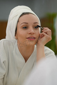穿着浴袍的白人美女在睫毛上涂睫毛膏。