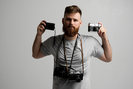 专业摄影机摄影照片_留着胡子的专业摄影师手里和肩上拿着一堆不同的老式旧相机。