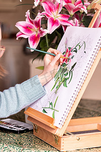 年轻的左撇子女孩在画架上用鲜花、紫色百合和水彩画静物画
