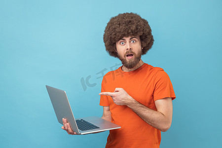 男人指着笔记本电脑屏幕，用震惊的表情看着相机，张大了嘴巴。