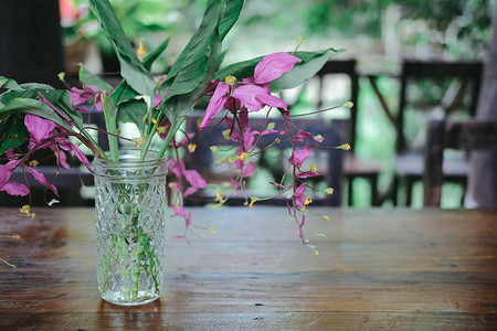 玻璃瓶装饰摄影照片_装饰在桌子上的玻璃瓶中的粉红色花朵和绿叶