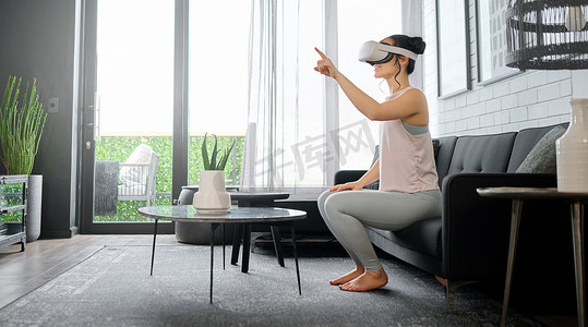真实宇宙摄影照片_一位女士在家中的客厅里使用耳机访问 3d 游戏，进行 VR、元宇宙和游戏。