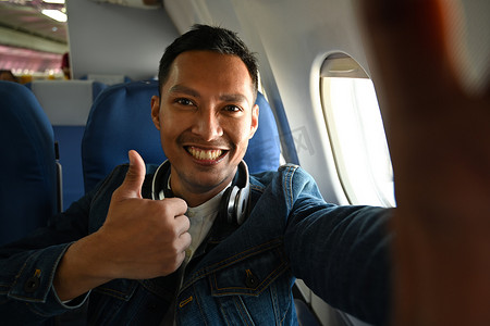 旅游博客摄影照片_坐在飞机上靠窗的快乐旅游博主拿着相机记录他的视频博客