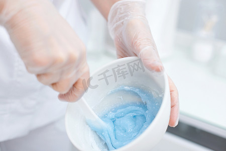 美容师手中装有蓝色藻酸盐面膜的碗。